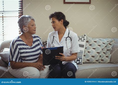 Female Doctor Interacting With Senior Woman In Living Room Stock Photo