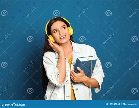 Young Woman Listening To Audiobook On Blue Background Stock Photo