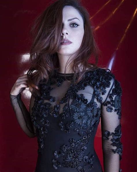 a woman in a black dress with sheer sleeves and flowers on her body is posing for the camera