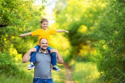 행복한 가족 아버지와 아들은 여름에 자연 속에서 걷습니다 아들은 아버지의 뒤에 앉아있다 프리미엄 사진