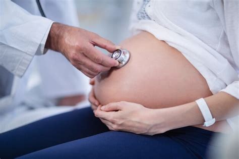 premium photo doctor examining pregnant womans belly with stethoscope in ward