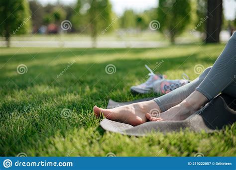 The Girl Sit On Yoga Mat Outdoor Feet On A Background Of Green Grass