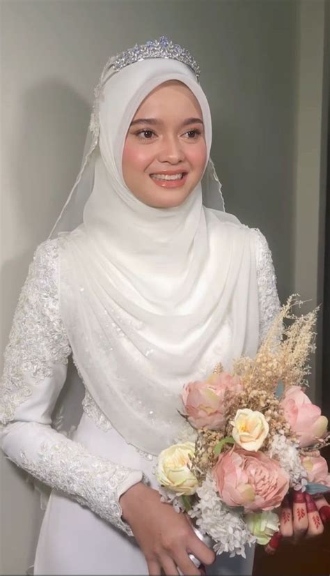 a woman wearing a white hijab holding a bouquet of flowers and smiling at the camera