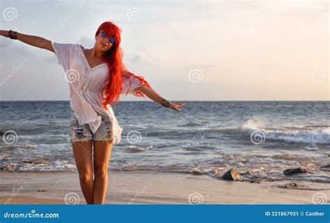 Carefree Red Haired Young Woman On A Tropical Beach At Sunset Standing With Her Arms Out Like An