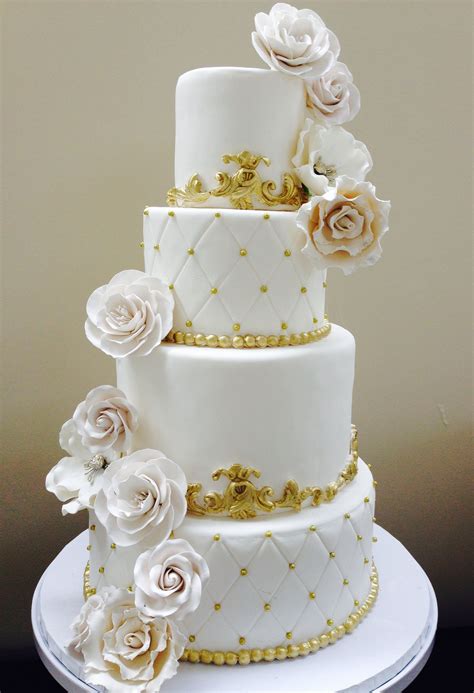 A Three Tiered Wedding Cake With White And Gold Flowers