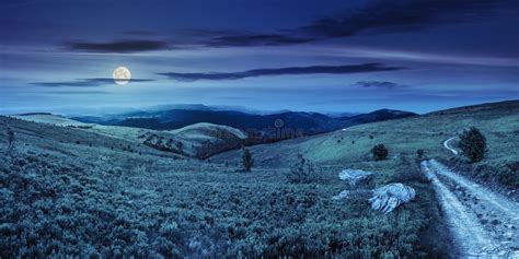 Road On Hillside Meadow In Mountain Panorama At Night Stock Photo