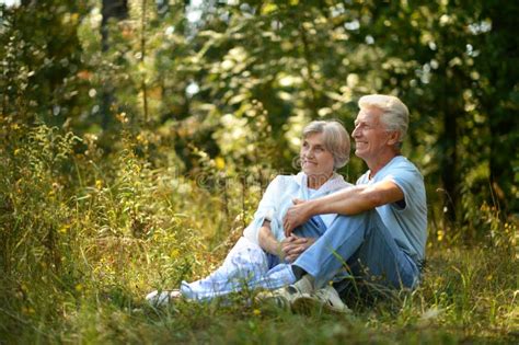 Portrait Of Nice Mature Couple Sitting On Green Grass In Summer Park