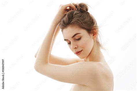 Portrait Of Young Beautiful Tender Naked Girl With Bun Posing In Profile Over White Background