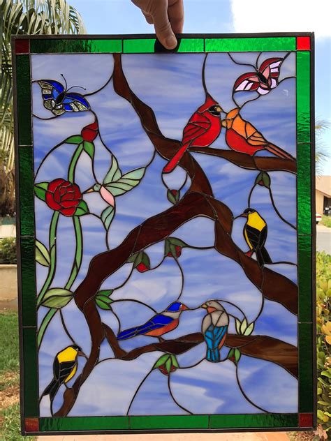 A Hand Holding Up A Stained Glass Window With Birds On Its Tree Branch