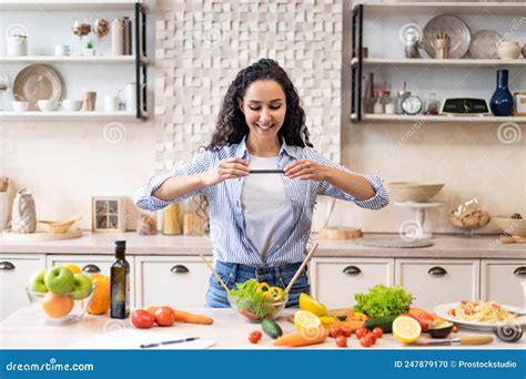 pretty latin female blogger making photo of salad for food blog standing in kitchen interior