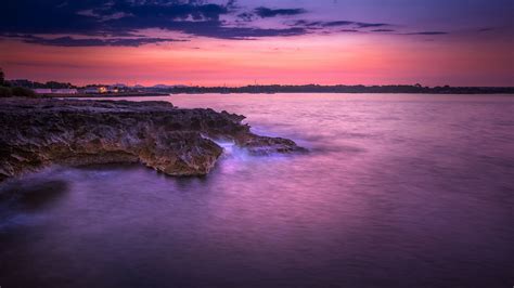 Rocks Sea Coast And Landscape View Of Buildings Under Purple Sky During