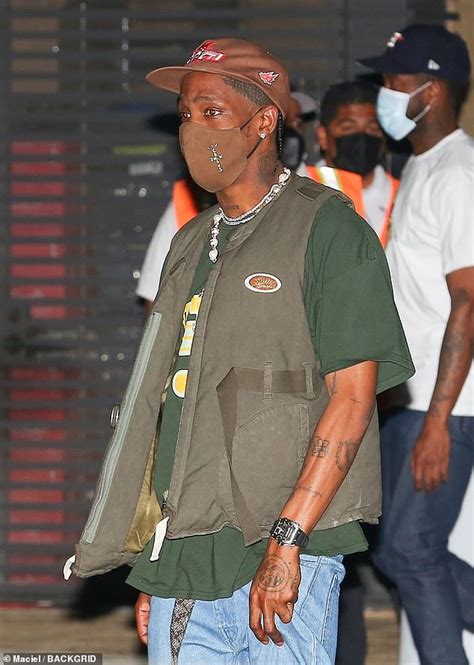 Travis Scott Rocks An Olive Green Vest And Light Wash Baggy Jeans As
