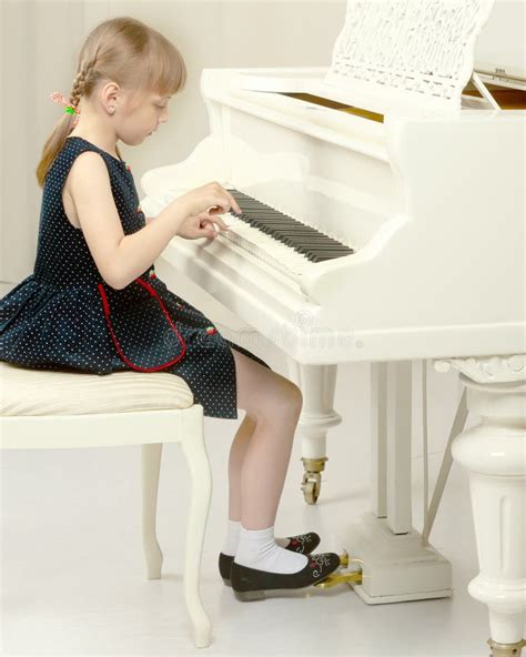 Beautiful Little Girl Is Playing On A White Grand Piano Stock Photo