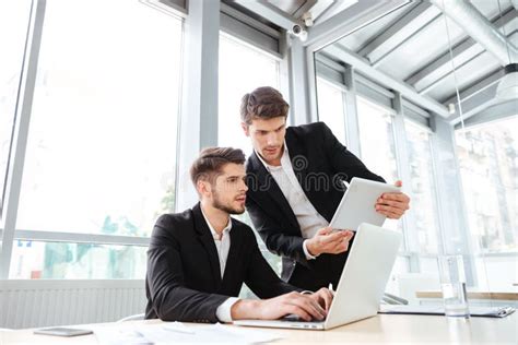Two Businessmen Using Laptop And Tablet In Office Together Stock Photo
