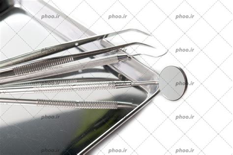 عکس با کیفیت پنس جراحی و سوند دندانپزشکی در کنار آینه مقعر و داخل ظرف فلزی از نمای نزدیک عکس