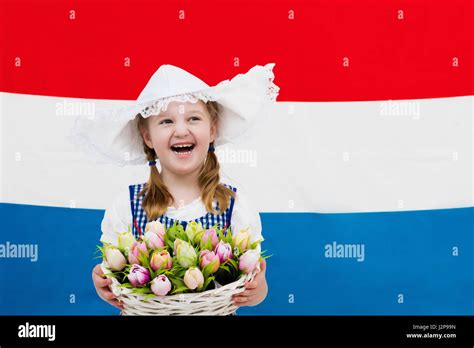 Little Dutch Girl Wearing Traditional National Costume Dress And Hat Holding Basket Of Tulips