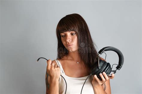 hermosa joven con tatuajes y perforaciones sosteniendo auriculares y un cable con un conector
