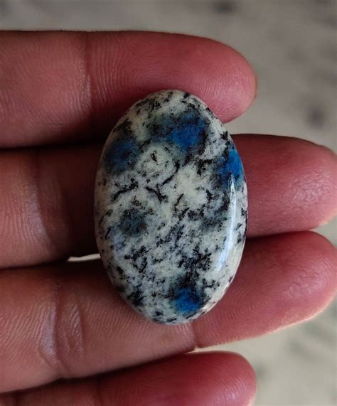 A Close Up Of A Persons Hand Holding A Stone With Blue Speckles