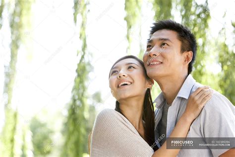 Young Chinese Couple Embracing And Looking Up In Park — Nature Willow