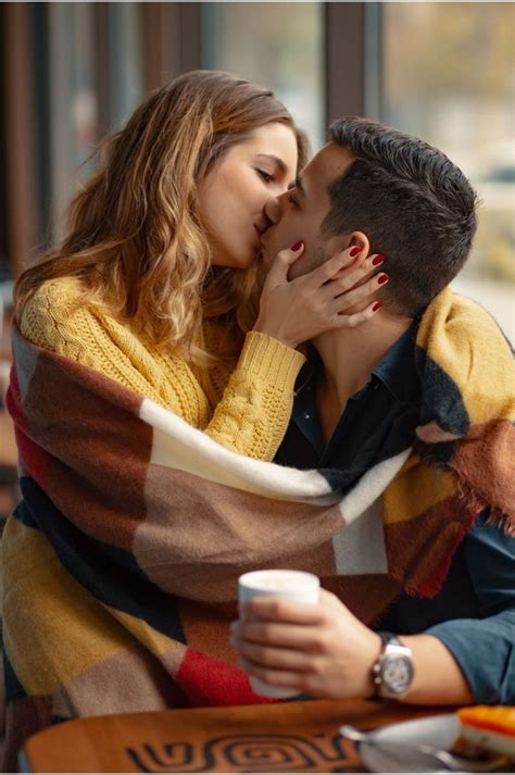 A Man And Woman Kissing While Sitting At A Table