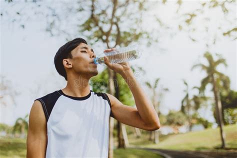 Sports Man Drinking Water After Exercising On Background Of Green Trees
