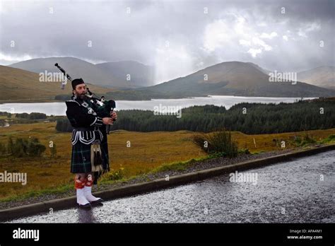 Piper in highland dress playing by the roadside over looking loch Tulla