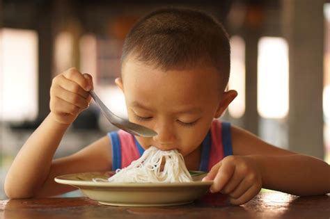 Premium Photo The Boy Uses A Spoon To Drop Food Noodles Into His