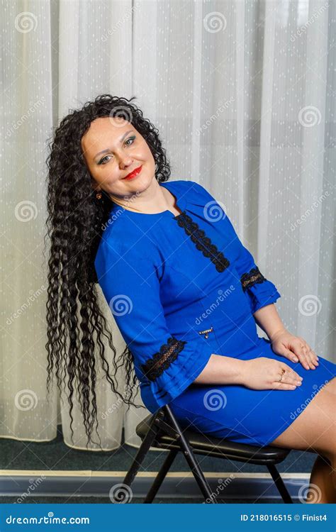 Curly Brunette Woman In Blue Sits On A Chair With Her Head Thrown Back Stock Image Image Of