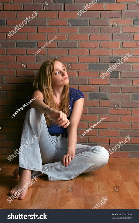 Woman Sitting Alone Against Brick Wall And Hard Wood Floor Stock Photo
