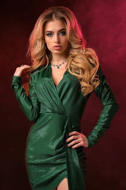 Mulher loira encaracolada em um vestido verde elegante e joias ela colocou a mão na cintura