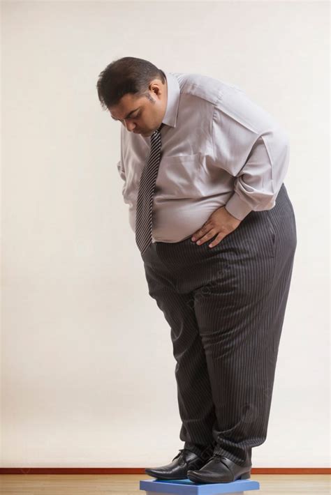 رجل سمين يرتدي ملابس رسمية يفحص وزنه على آلة قياس الوزن صورة الخلفية والصورة للتنزيل المجاني