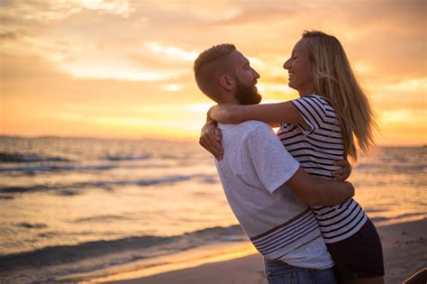 Cheering Couple Being Affectionate On Beach At Sunset Stock Photo