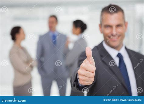 Smiling Manager Showing Thumb Up With Employees In Background Stock