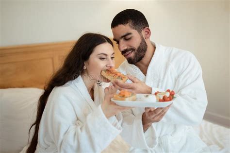 Husband Feeding Wife Giving Her Sandwich Having Breakfast In Bedroom