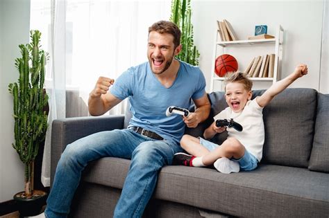 Padre Y Su Pequeño Hijo Jugando Videojuegos Juntos En El Sofá En Casa