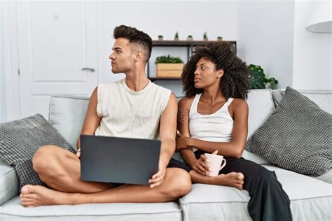 Young Interracial Couple Using Laptop At Home Sitting On The Sofa