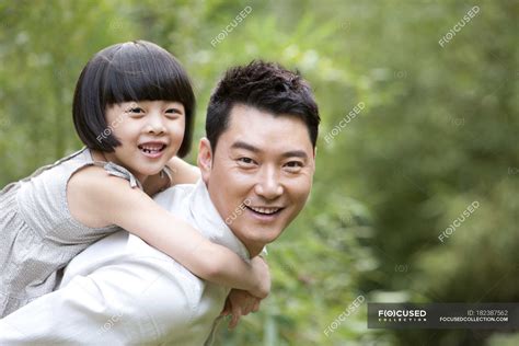 Chinese Father Giving Daughter Piggyback Ride In Garden — Casual
