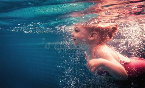 Happy Child Swimming Underwater In Swimming Pool During Diving Training