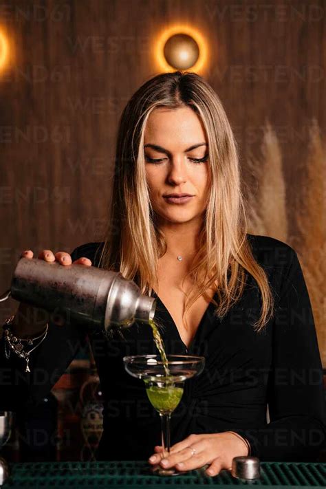 Beautiful Blonde Young Female Bartender In Stylish Outfit Pouring Alcohol Cocktail From Shaker