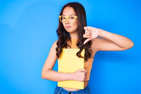 Young Beautiful Chinese Girl Wearing Glasses Holding Book With Angry