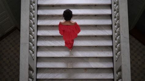 Woman Walking Up Stairs While Wearing A Formal Red Dress Then Looking