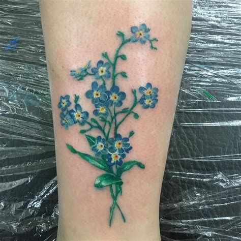A Small Blue Flower Tattoo On The Right Leg With Green Stems And White