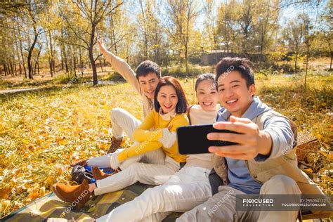 vier junge lächelnde asiatische freunde machen selfie mit smartphone im herbstlichen wald