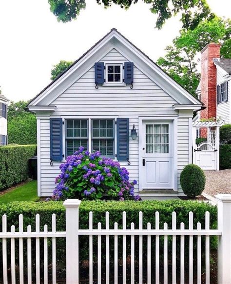 A White House With Blue Shutters And Purple Flowers In The Front Yard