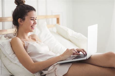 Woman Typing On Laptop From Her Bed By Lumina