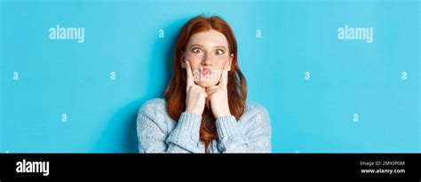 Close Up Of Funny Redhead Teen Girl Making Faces Squinting And Pocking Cheeks Standing Against