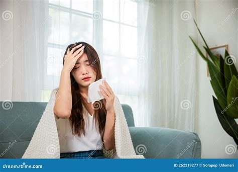 Sick Woman Sitting Under Blanket On Sofa And Sneeze With Tissue Paper