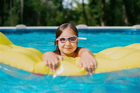 Young Girl With Swim Goggles Holding On To A Yellow Floating Device By Stocksy Contributor