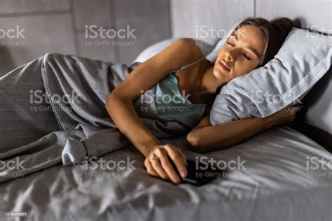 Young Woman Sleeping In Bed Being Woken By Mobile Phone Stock Photo
