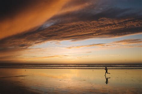 Side View Of Mid Adult Nude Womans Silhouette Running On Beach Under Dramatic Sky At Sunset